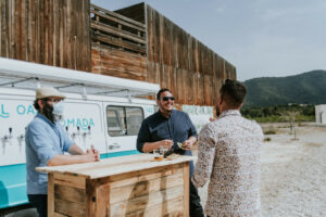 Varias personas disfrutando unas cervezas en el exterior de una casa rural con la tap truck de El Oasis Nomada y una barra de bar de madera