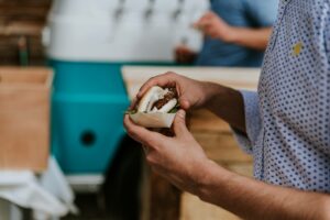 Primer plano de un hombre sosteniendo una hamburguesa. De fondo, la tap truck de El Oasis Nómada